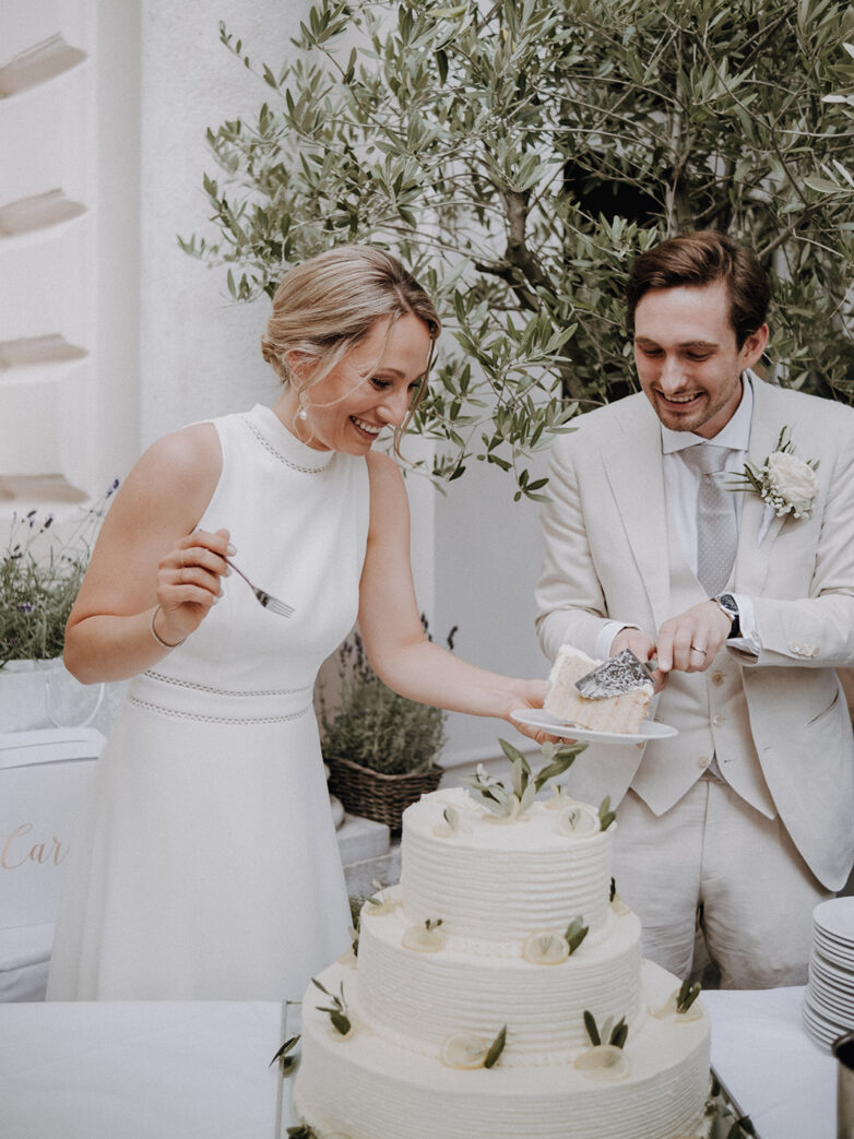 Bride and groom joyfully cutting their wedding cake at the Hotel Regina in Vienna, surrounded by lush greenery and romantic ambiance.