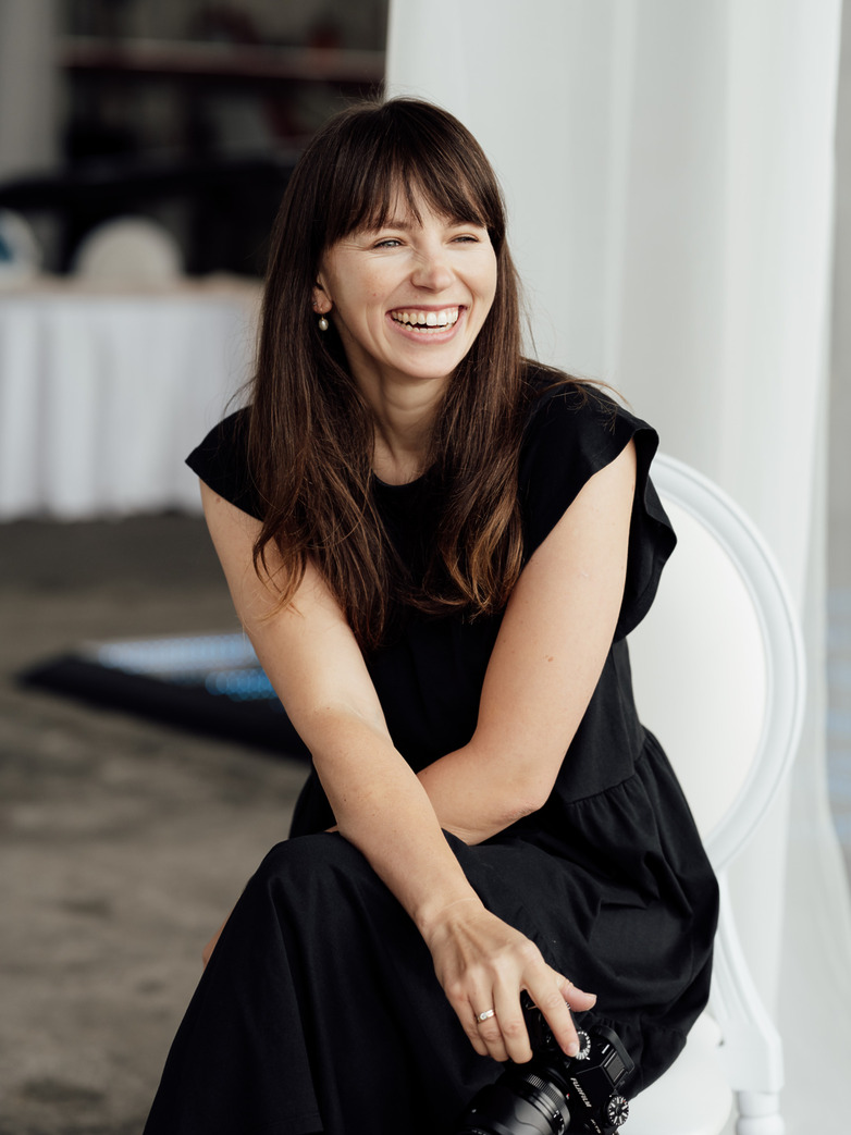 Wedding photographer in Vienna smiling while seated with her camera, natural light portrait for modern editorial wedding branding.