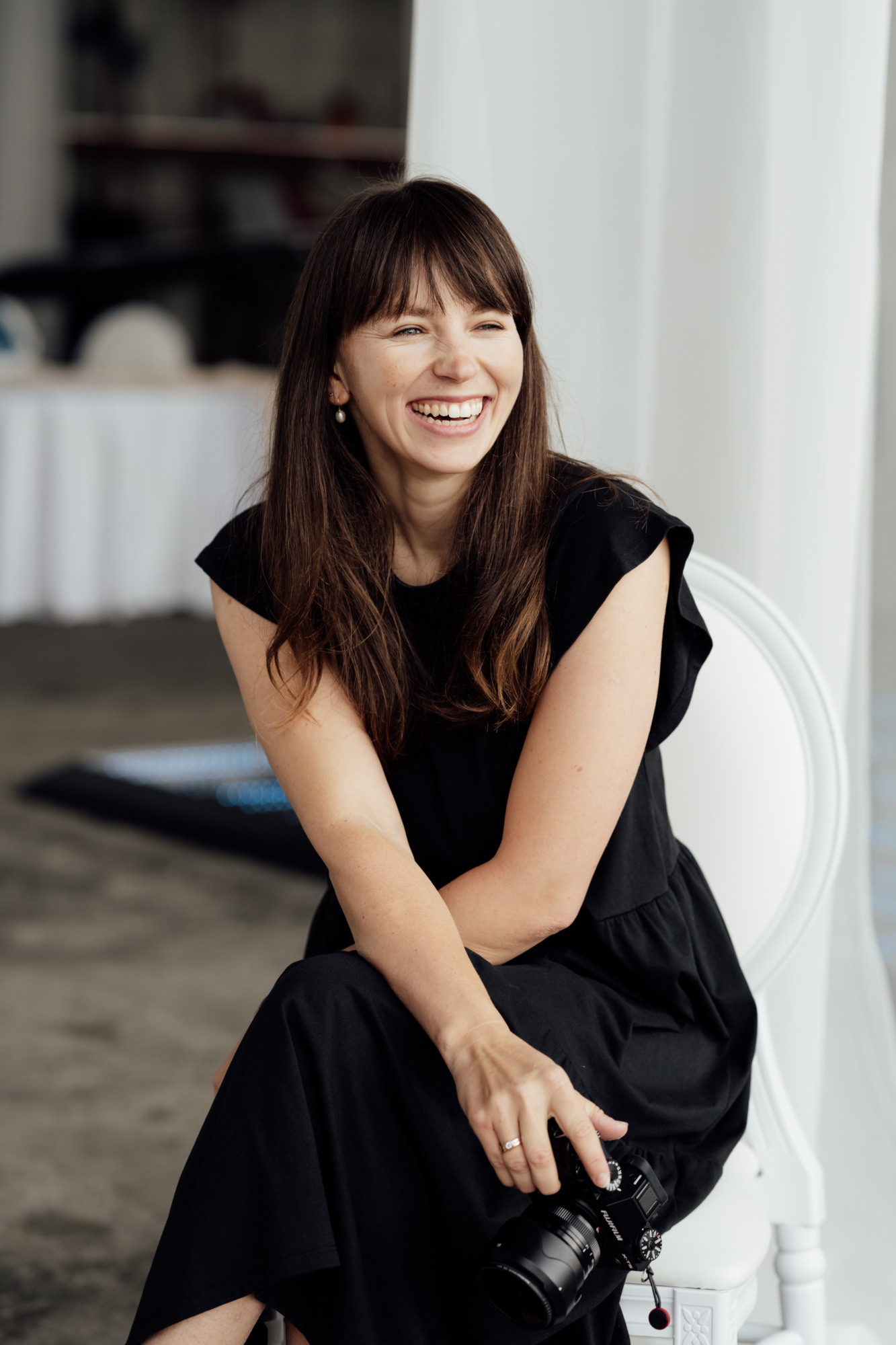 Wedding photographer in Vienna smiling while seated with her camera, natural light portrait for modern editorial wedding branding.