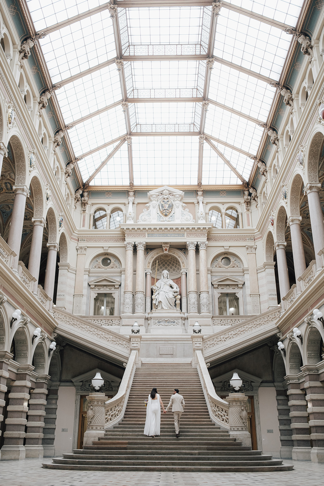 Bride and groom standing on a grand staircase inside a historic Vienna palais with elegant architectural details