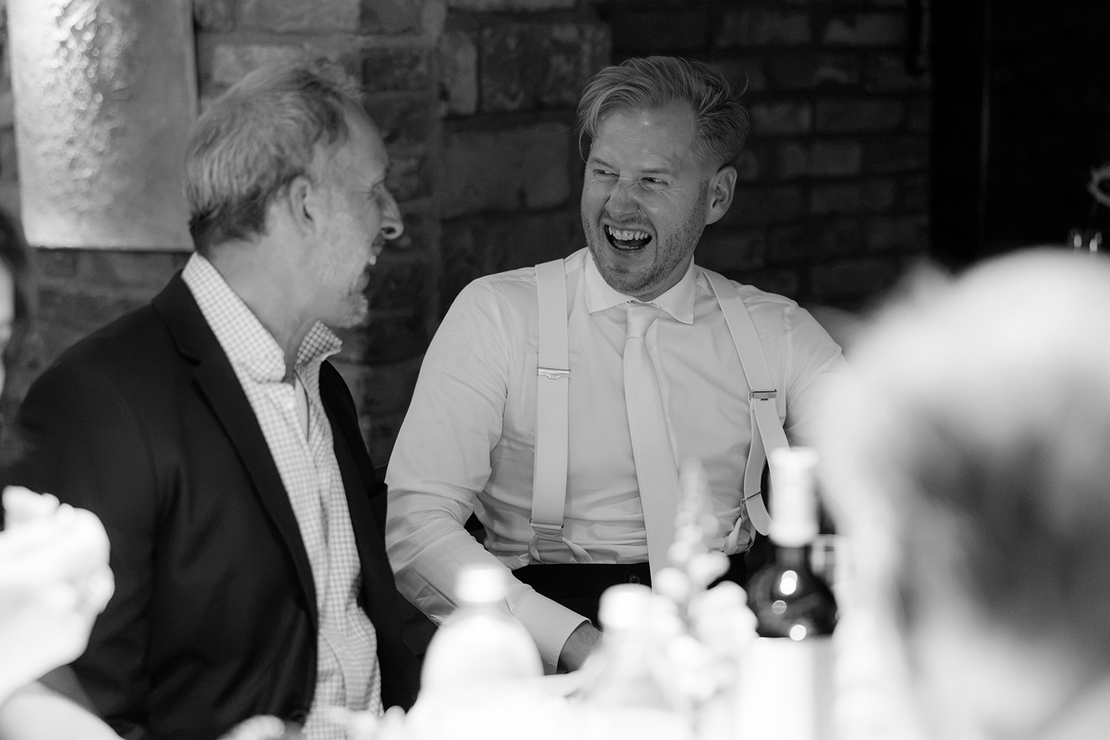 Black and white photo of the groom laughing with a guest at dinner during a wedding Am Reisenberg in Vienna