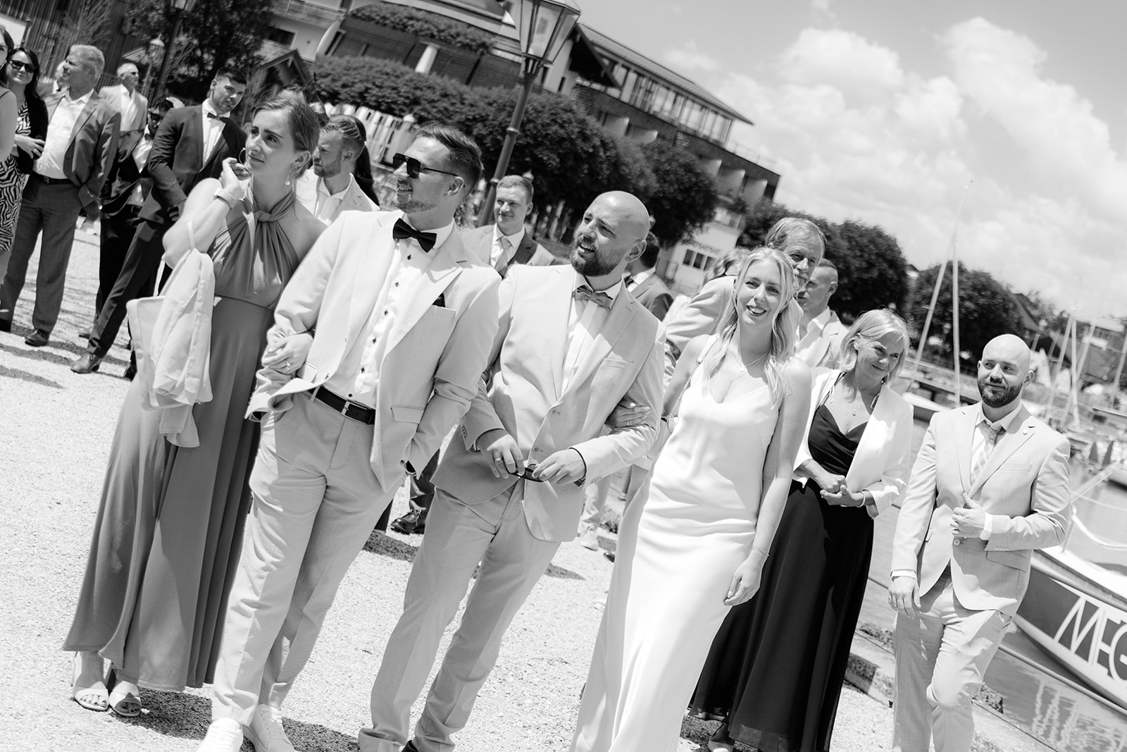 Black and white photo of the wedding party walking along the harbour at Mattsee, Salzburg