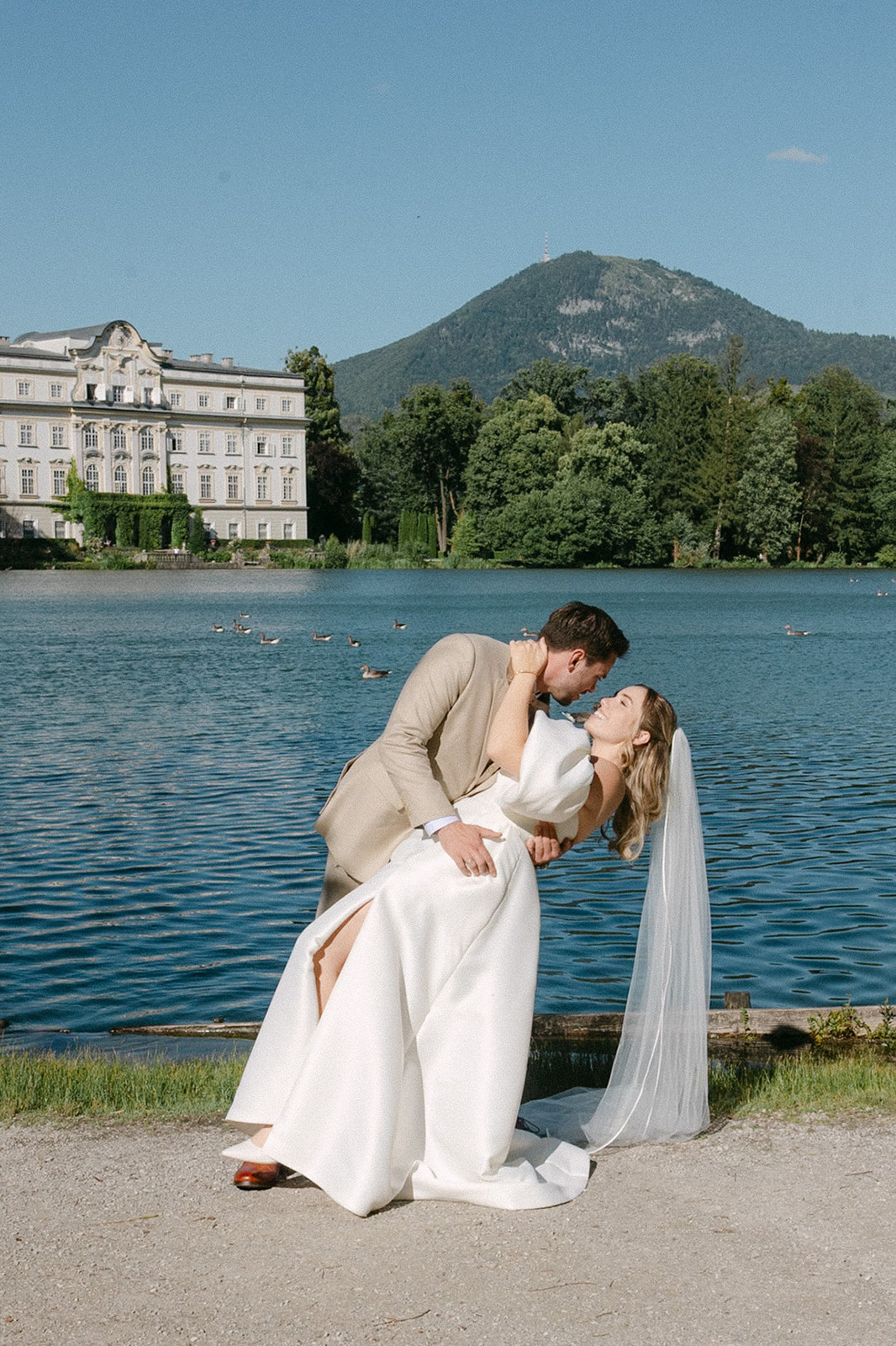 Groom dipping the bride for a kiss by the Leopoldskroner Weiher with Schloss Leopoldskron in the background, Salzburg