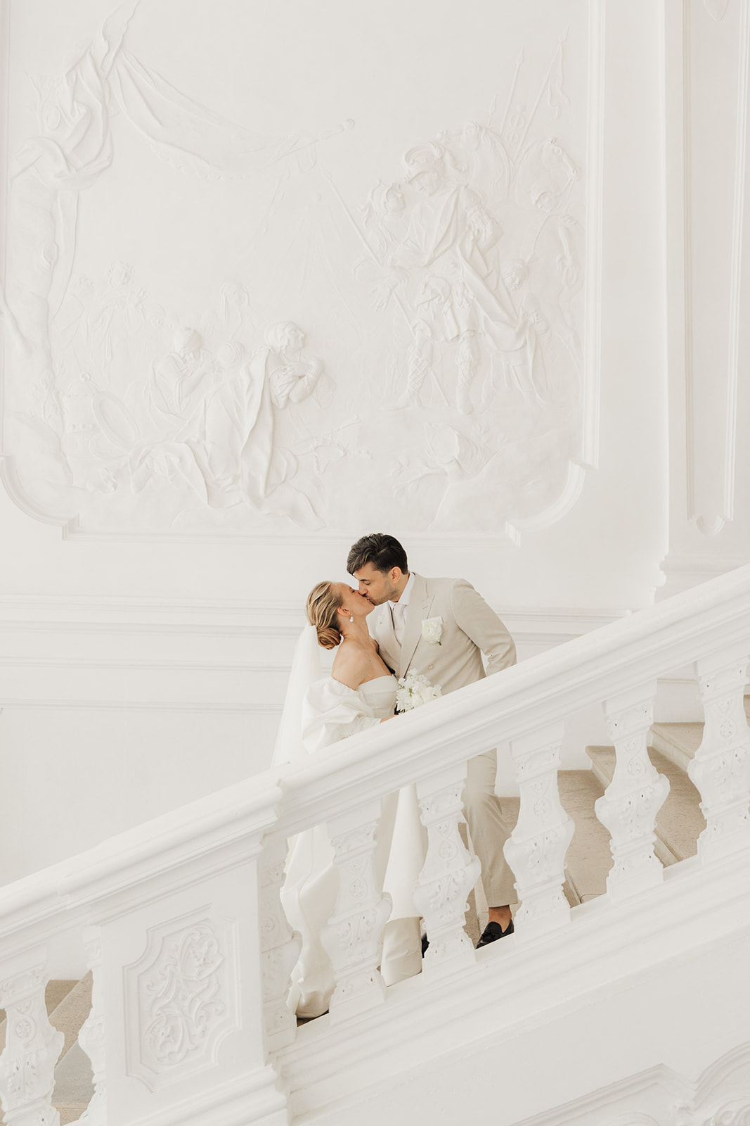 Bride and groom kissing on the white marble staircase of the Upper Belvedere palace in Vienna
