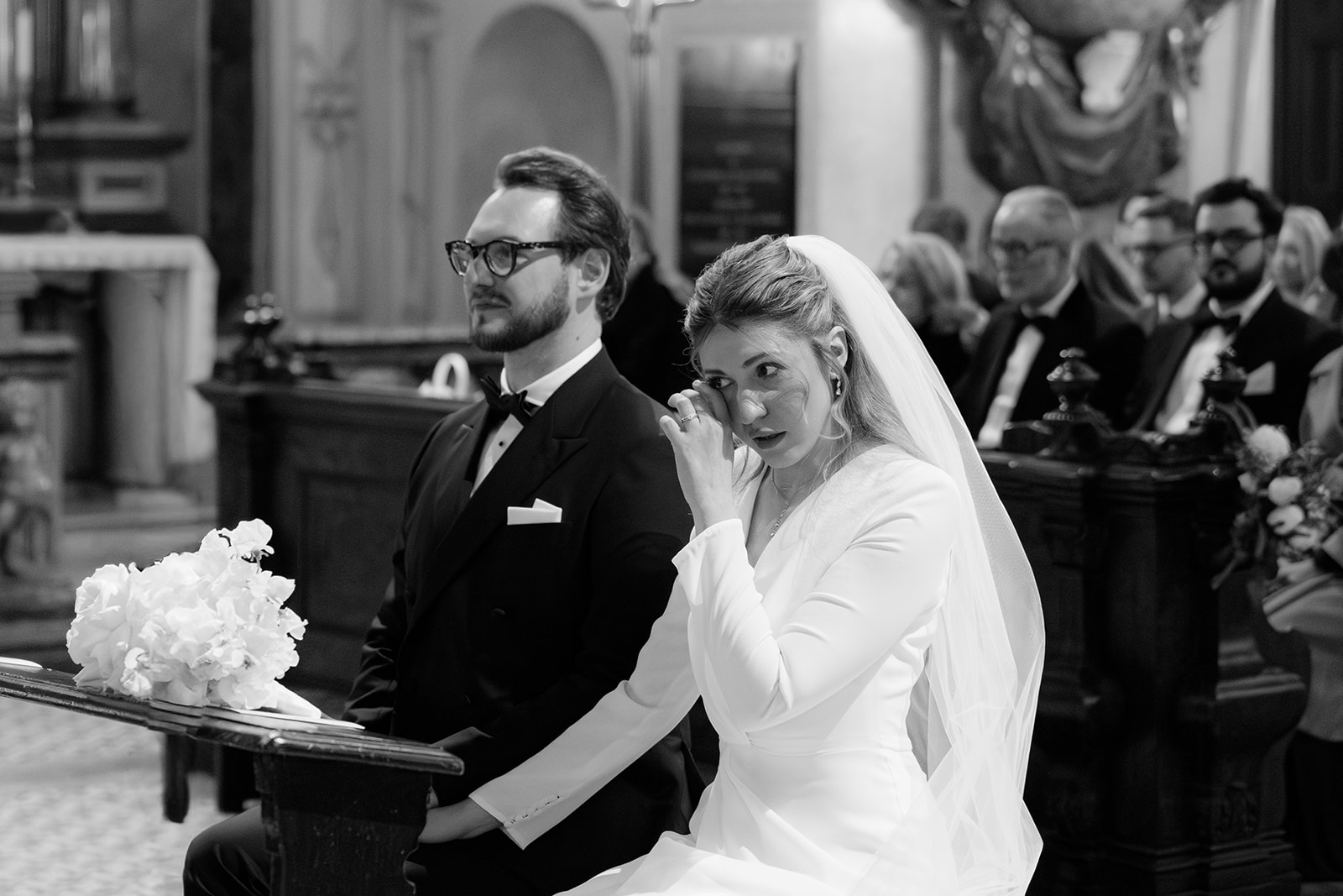 Black and white photo of a bride wiping away tears next to the groom during a church wedding in Vienna