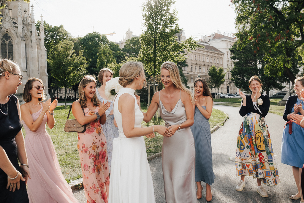 Bride celebrating with her friends in the park in front of the Votivkirche in Vienna